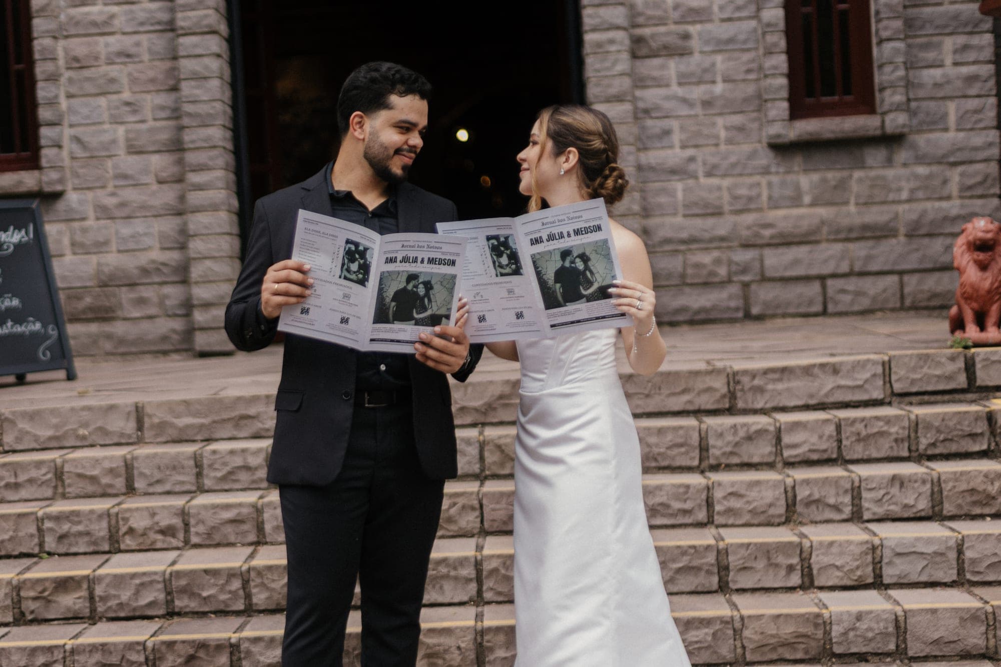 Casal lendo o jornal do casamento na escadaria