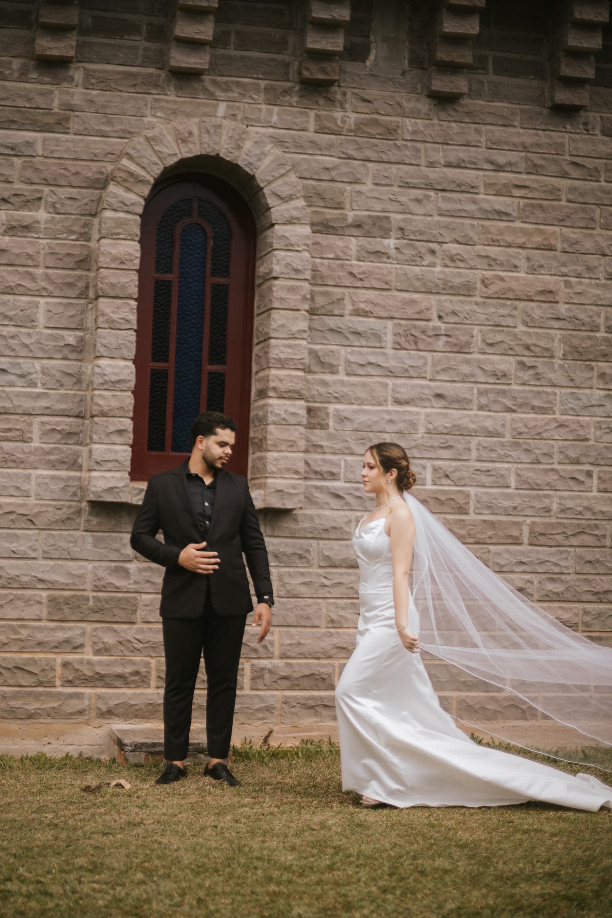 Casal em frente à parede de pedra do castelo, véu estendido no chão