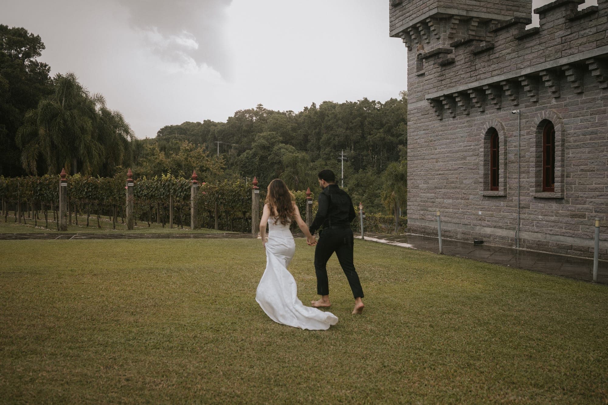 Casal correndo de mãos dadas no gramado, com o castelo ao fundo