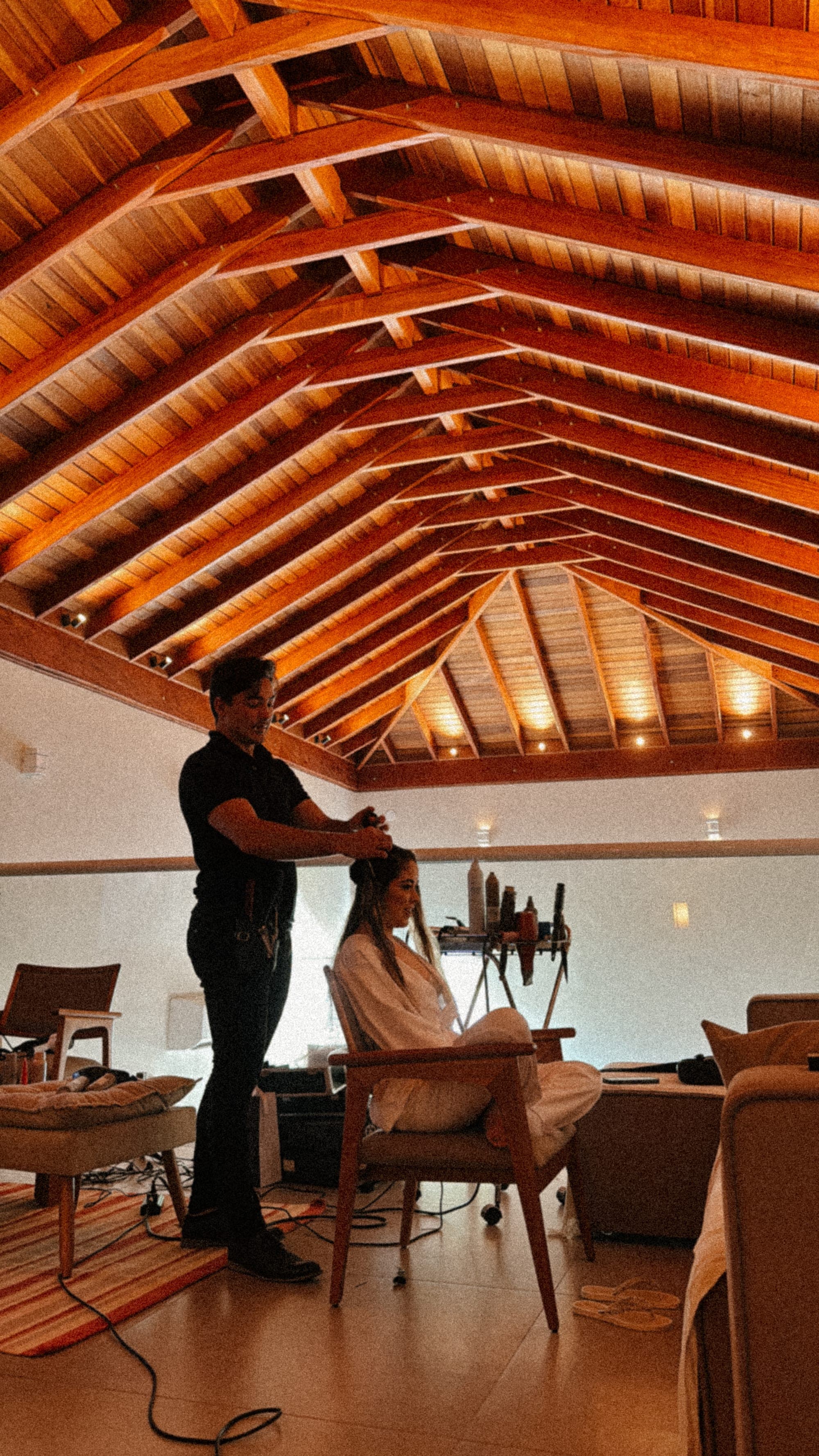 Cabelo sendo finalizado sob o telhado de madeira, em luz quente