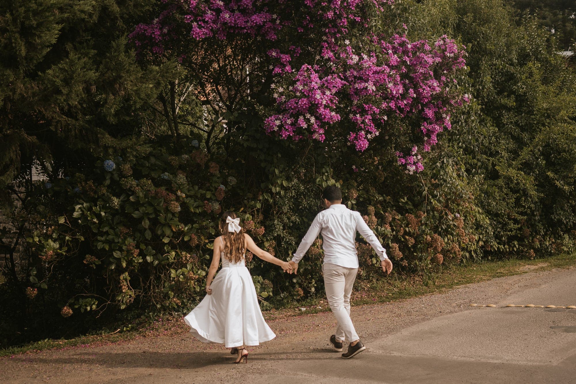 Casal caminhando de mãos dadas ao lado da árvore florida